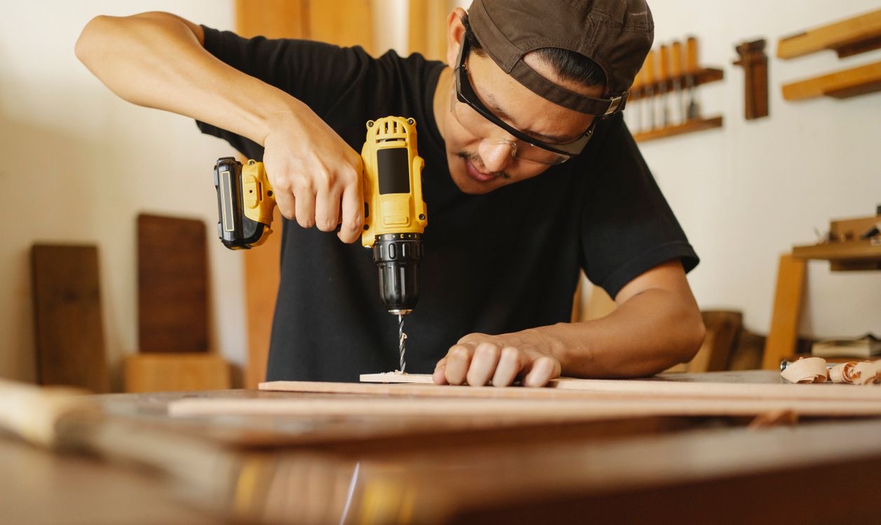 A woodworker using a cordless drill at a workshop bench