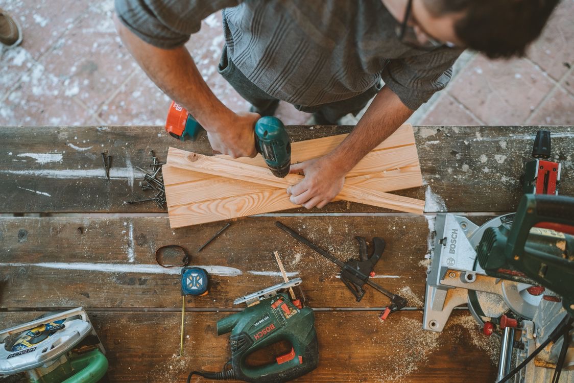 A carpenter fastening wood at a bench surrounded by project tools
