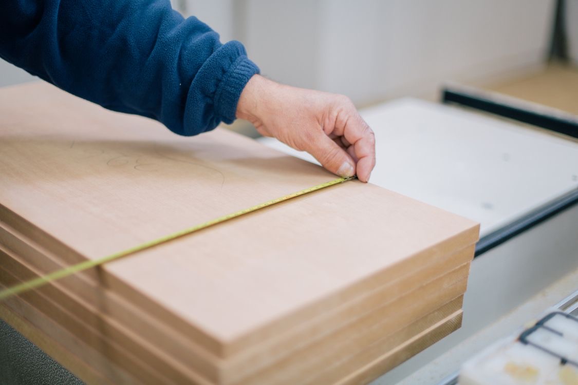 A person stretching a tape measure across a wooden panel in a workshop