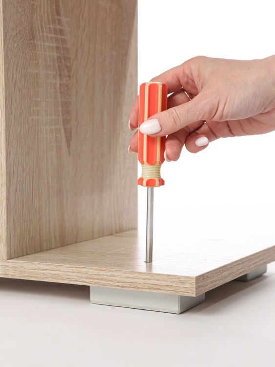 A hand using a manual screwdriver vertically while assembling wooden furniture