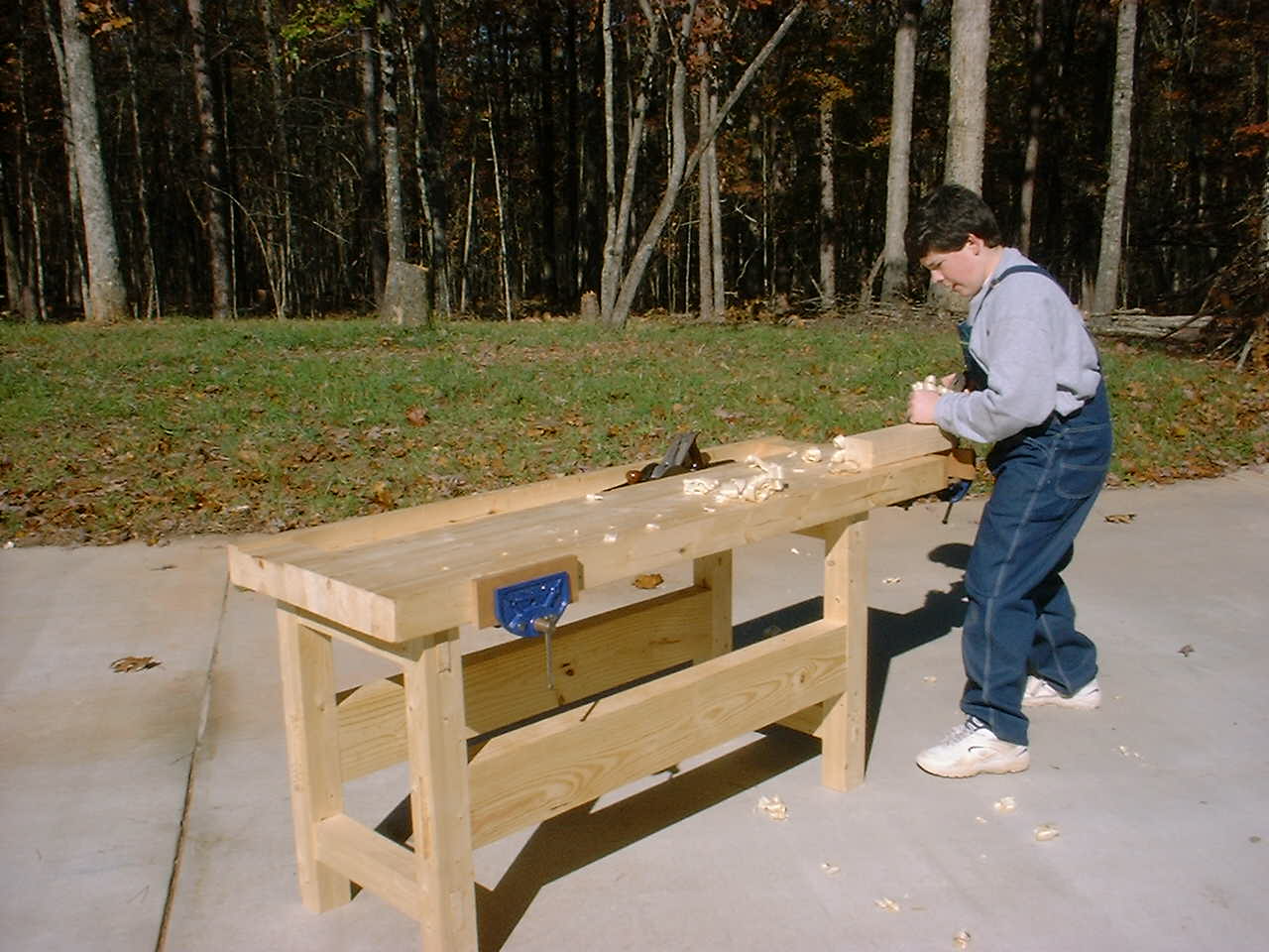 A woodworker using the end vise of a wooden workbench outdoors