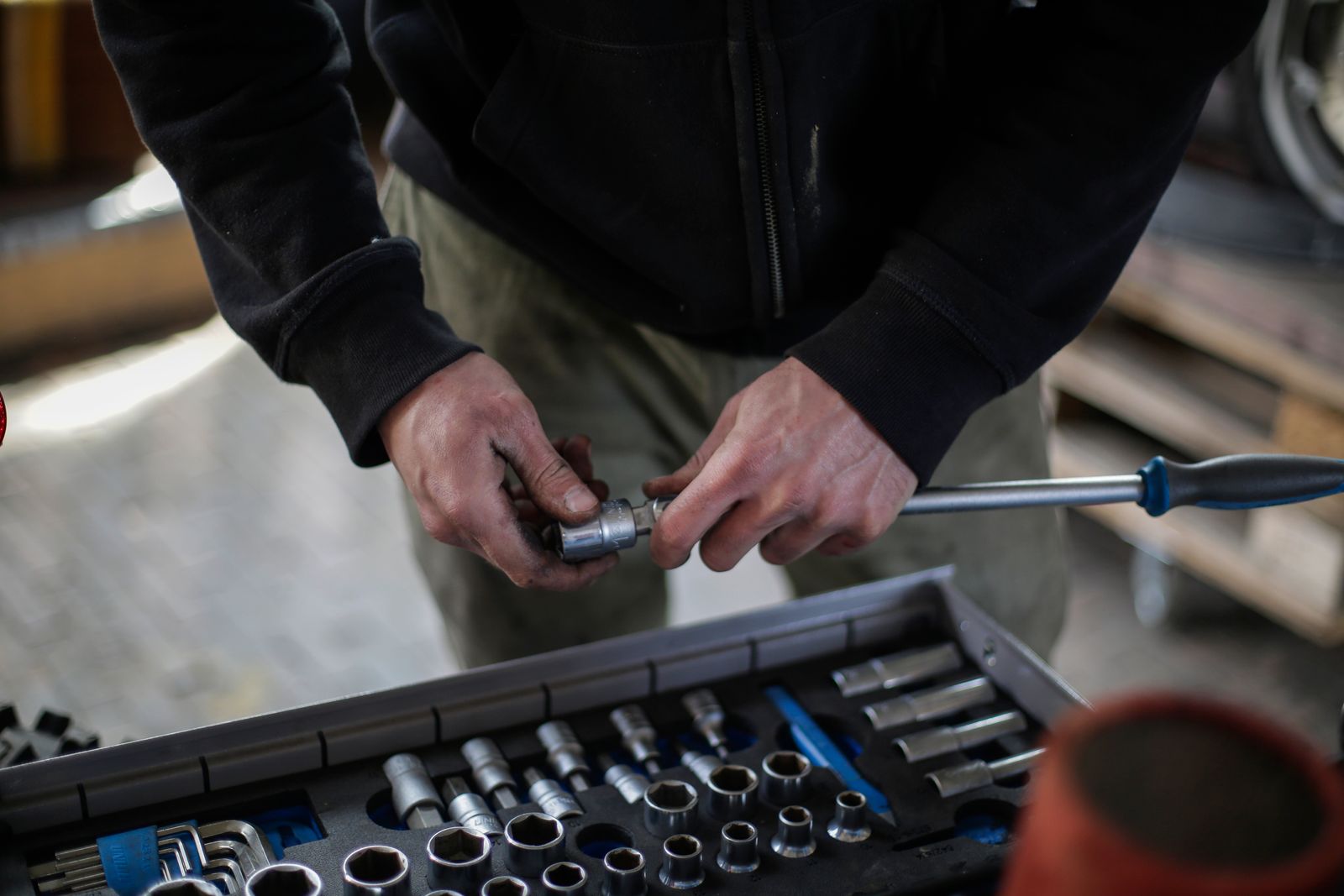 A mechanic fitting a socket onto a hand tool above an organized socket tray in a workshop