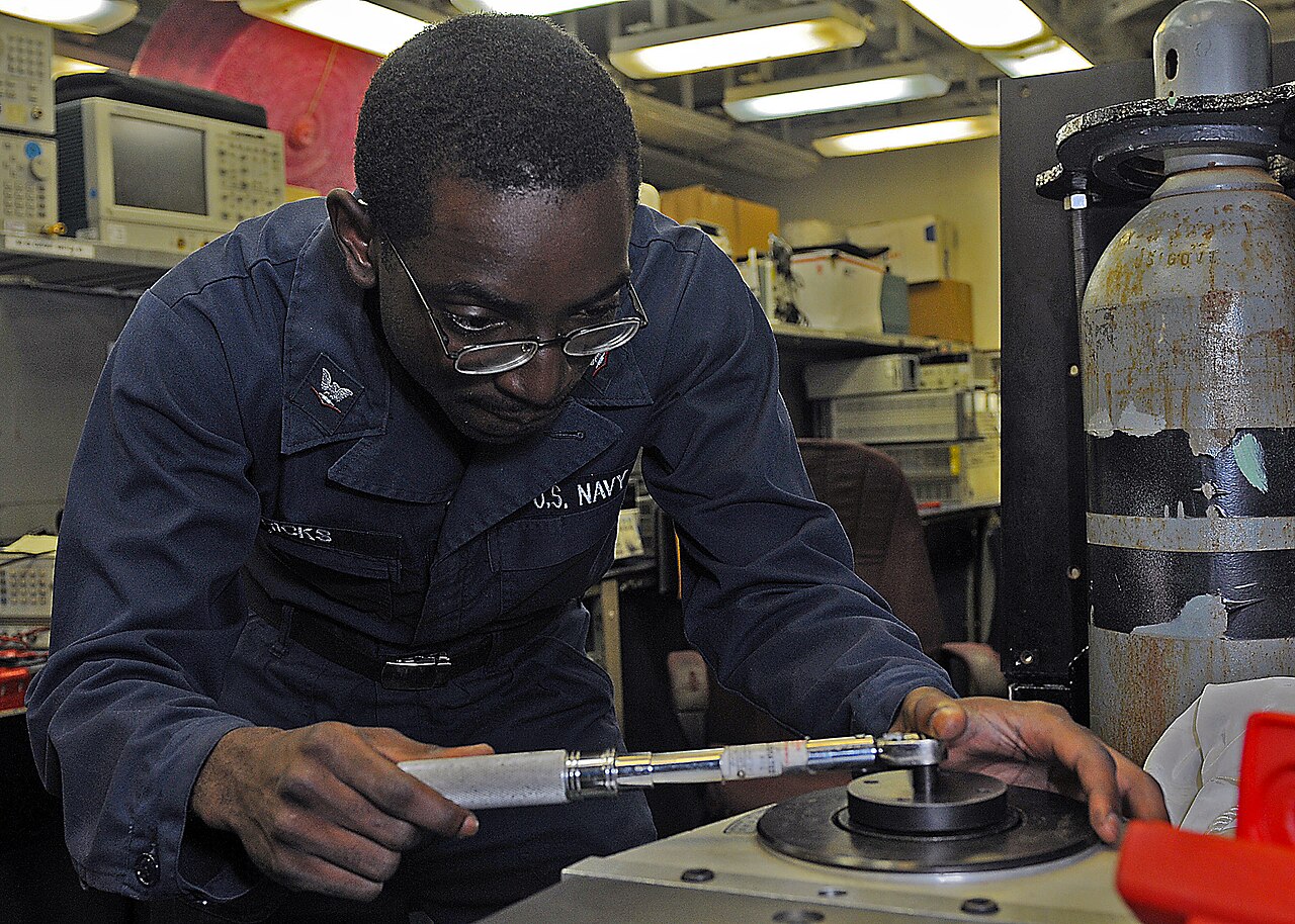 A U.S. Navy technician checking a torque wrench on a calibration instrument at a laboratory bench