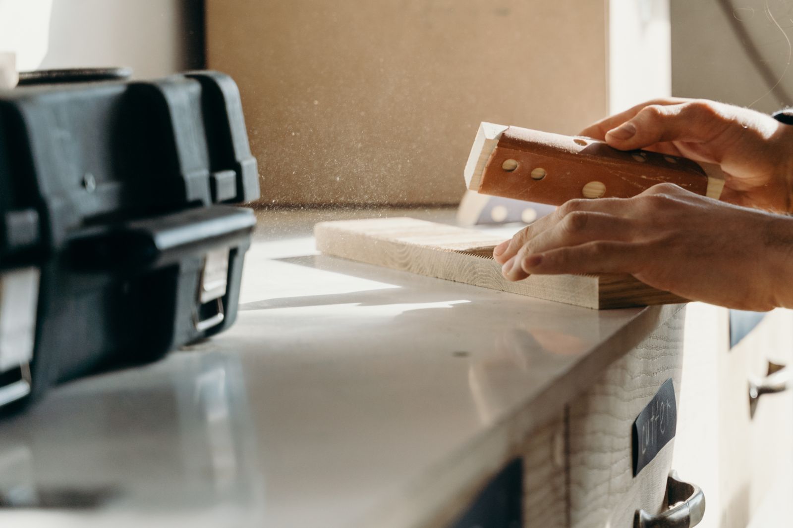 Hands sanding the surface of a wooden piece at a workshop bench
