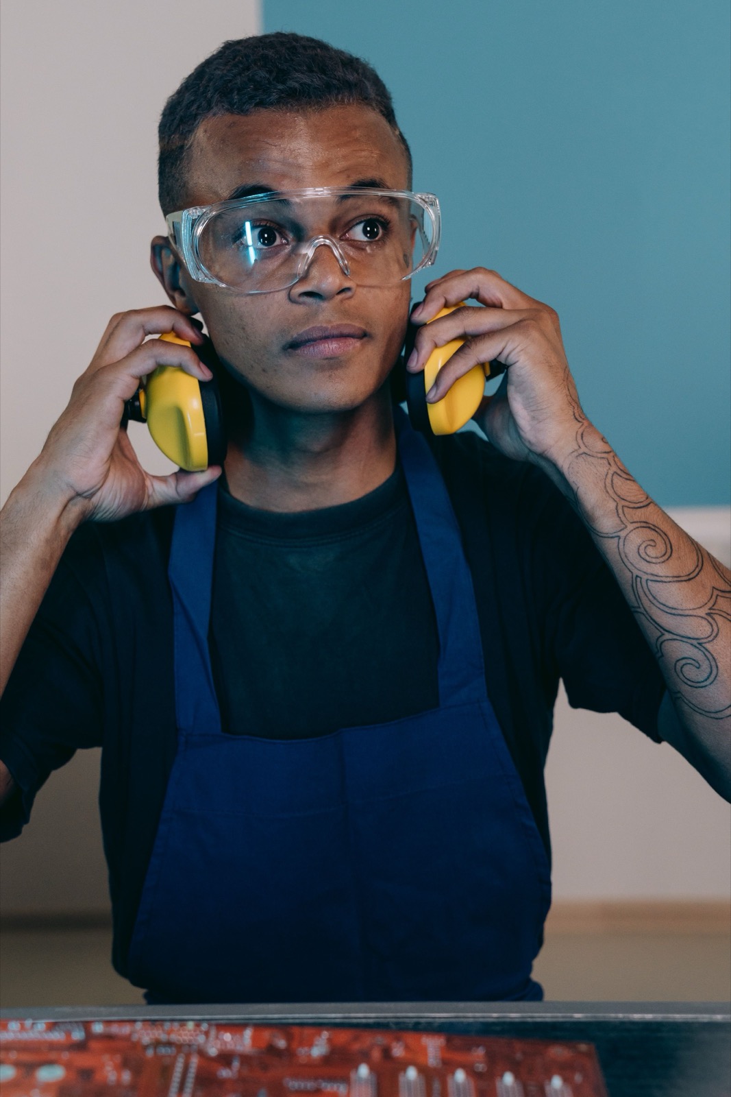A worker at a workshop bench putting on earmuffs while wearing protective eyewear