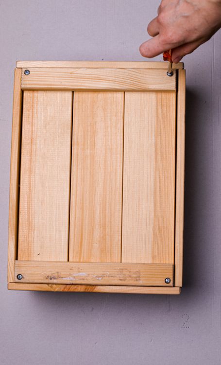 A hand using a manual screwdriver on a wooden box